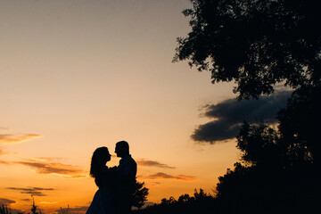 Obraz premium silhouettes of a happy young couple guy and girl on a background of orange sunset