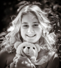 Emotional smiles' girl hugging her teddy bear. Young cute girl embracing her fur teddy bear. Little girl in love with her stuff toy. Black and white.