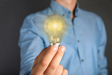 Man holding glowing light bulb on grey background, closeup