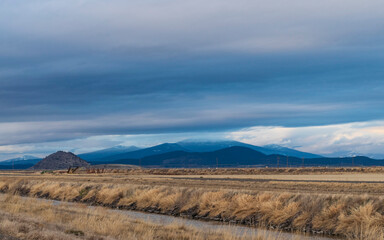 A mixture of blue clouds hovers over mountains and fields in Northern California on the Lower Klamath Wildlife Refuge.