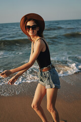 cheerful woman in sunglasses and a hat walks along the ocean