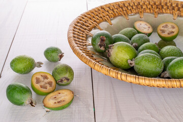 Several fragrant sweet feijoa fruits with ceramic dishes, close-up, on a wooden table.