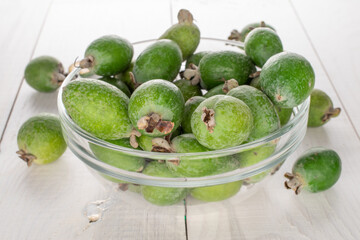 Several fragrant sweet feijoa fruits with glassware, close-up, on a wooden table.