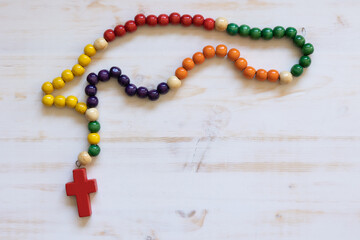 Rosary with colourful beads and cross on a white wood background with copy space
