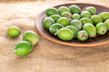Several fragrant sweet feijoa fruits with earthenware on sacking, close-up.
