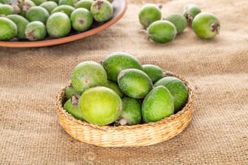 Several fragrant sweet feijoa fruits with straw dishes on sacking, close-up.