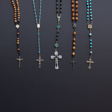 Multiple rosaries hanging on a black background