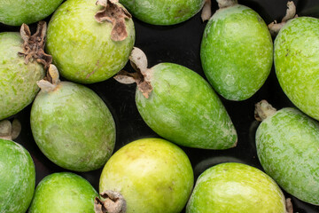 Several fragrant sweet feijoa fruits in a black bowl, close-up, top view.