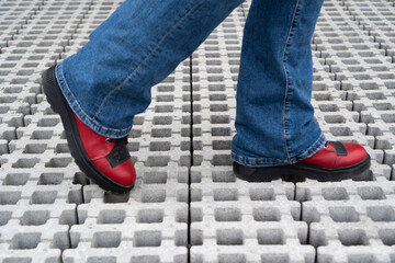 Legs walking on the paving slabs. Feet in red shoes on the road. Cantry red boots walking on pavement. Blue jeans