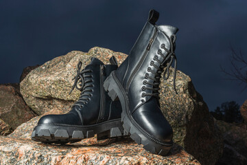 Leather black women's rough boots with thick soles on a background of stones