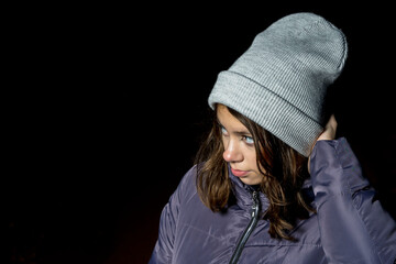 Portrait of a cute fashionable Caucasian girl with dark hair dressed in a modern warm knitted hat and a purple down coat