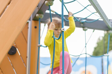 child girl climbs the rope ladder in the open playground on a summer day. focus on the rope. baby in blur