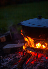 Vertical photo of a cauldron with food on fire in nature. Orange campfire for outdoor cooking