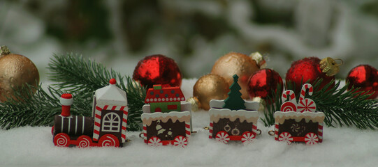 Toy locomotive in the snow against the background of Christmas tree branches and Christmas balls, the background is blurred. Christmas, New Year banner, postcard, flyer, layout design, narrow image
