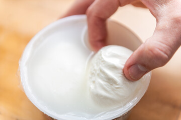Obraz na płótnie Canvas Macro closeup of hand holding fresh burrata mozzarella Italian cheese in storebought plastic container with brine and white color