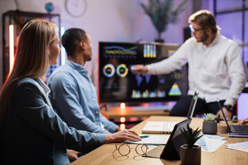Caucasian man showing on monitor financial statistic of company for multicultural partners at modern office. Business people using modern technology for work. Conference process.