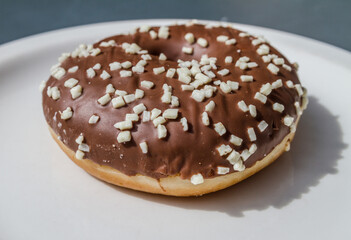 Delicious glazed doughnut on a white plate. Donut with chocolate frost and sprinkles.