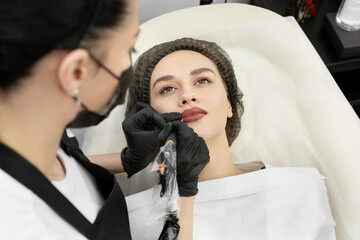 Close-up of the permanent makeup procedure. Lip makeup in the cosmetologist's salon.