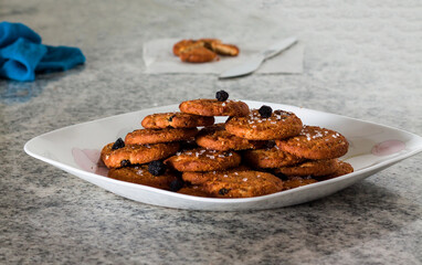 Selective focus on a stack of chocolate chip cookies.Served in a white plate topped with berries and isolated on a blur white marble background.Front view,closeup of delicious,crunchy cookies.

