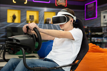 Teenage boy wearing virtual reality glasses, who holds on to the steering wheel and plays a...