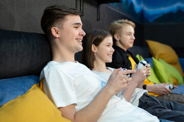Group of friends of teenagers, boys and girls playing video games on a console in a game club.