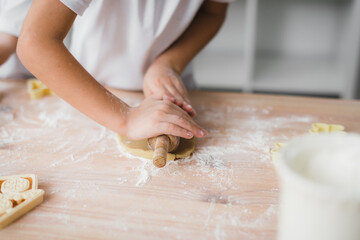Cooking and home concept - close up of kid hands roll out cookie dough at home in kitchen.