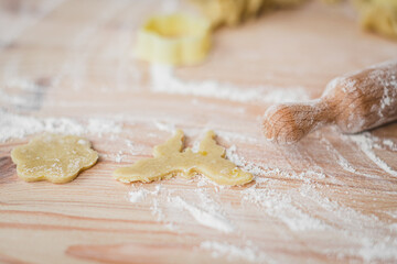 Close-up of blank cookies from raw dough of different shapes on the kitchen table, strewn with flour.