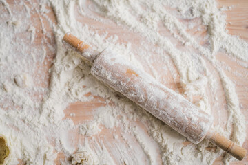 Close-up wooden rolling pin lying on the kitchen table with flour.