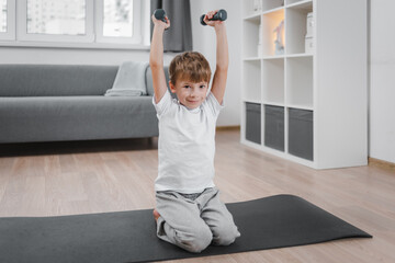 Portrait of boy child exercising with dumbbells at home. A child who strengthens the muscles of the arms. The concept of strengthening the health and recreation of children.
