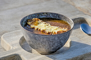 Bowl of onion soup, au gratin with cheese on bread on a wooden table on a sunny terrace of an outdoor cafe