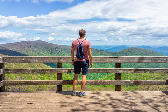 One young man with drawstring bag backpack standing on observation overlook deck wooden platform at Wintergreen ski resort town on nature Highlands leisure hiking trail, Virginia
