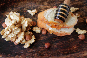 honey spoon with natural honey on a slice of bread in a wooden plate, decorated with kernels of nuts.