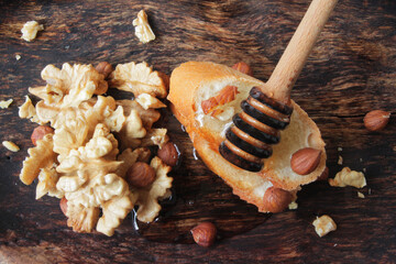 honey spoon with natural honey on a slice of bread in a wooden plate, decorated with kernels of nuts.