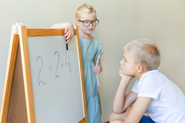 Children play school. A school-age boy, with his cheek propped on his hand, listens thoughtfully to the explanations of a teacher girl in big glasses.