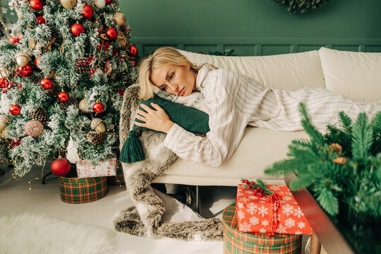 Frustrated depressive sad sick woman in pajamas lies on the sofa in christmas alone. Holidays alone at home.