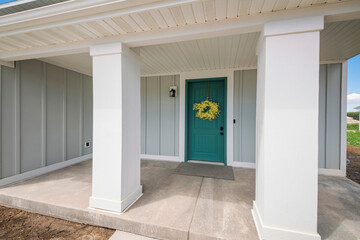 Front porch of a house with blue green front door and yellow wreath