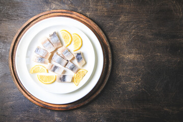 Salted herring with lemon on plate on wooden background with copy space. Marinated sliced fish. Food with healthy unsaturated fats, Omega 3. Top view, flat lay