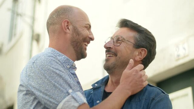 Medium shot of happy guys touching each other with tenderness. Handsome bearded men looking at each other, hugging, kissing and spending time together outside. LGBT, romantic relationship concept