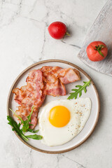 English breakfast. Egg and fried bacon. A cup with tomatoes. Serving breakfast on a marble table. Fried egg.