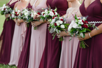 Bridesmaids in pink and claret-colored dresses holding their wedding bouquets of flowers with white and red roses Closeup of bridesmaids holding flowers at the wedding day holding flowers in hands
