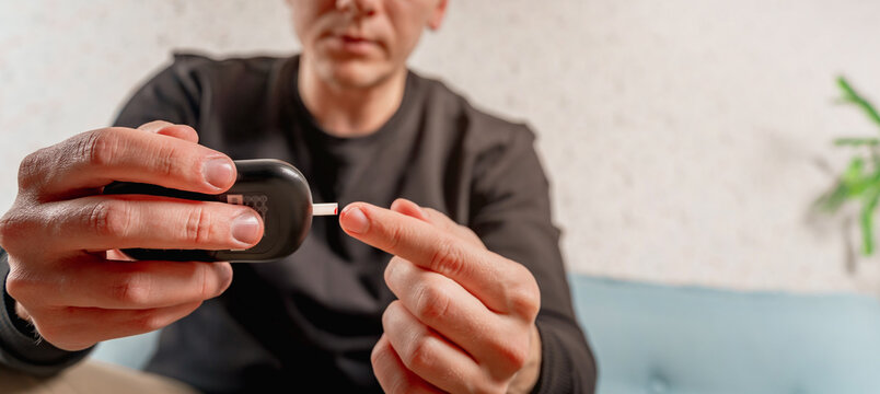 A man at home uses a glucose meter to measure blood glucose. Piercing a finger with a needle