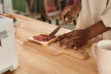 Close-up of African woman making toast with jam at the table for breakfast in the morning