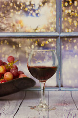 Bunch of purple grapes , glass of red wine stand on wooden table against window. Red grape on a plate. Harvest in vineyard. Romantic evening at home. Still Life with fruits and alcoholic beverage.
