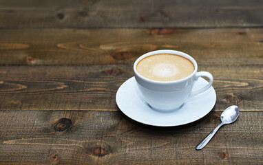 Close up white cup with cappuccino, wooden table, coffee, space for your text or logo 