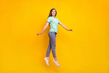 Full length photo of funny brunette hairdo young lady jump wear t-shirt jeans sneakers isolated on yellow background