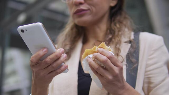 Busy woman quickly eating fast food, scrolling smartphone, unhealthy lifestyle