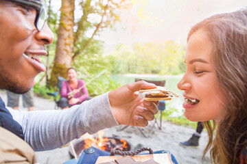 Obraz premium Young Adult African American Man Feeding Hispanic Girl A Smore at Campfire Outdoors.