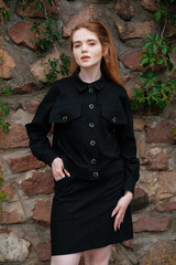 A girl in a black suit standing near a stone wall. Outdoor female portrait.