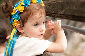 A small child with pigtails in national Ukrainian folk decoration looks through the bench
