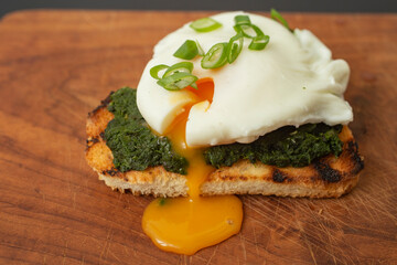 Selective focus close up , of a poached egg on a slice of toasted bread with spinach and spring onion, on the wooden table